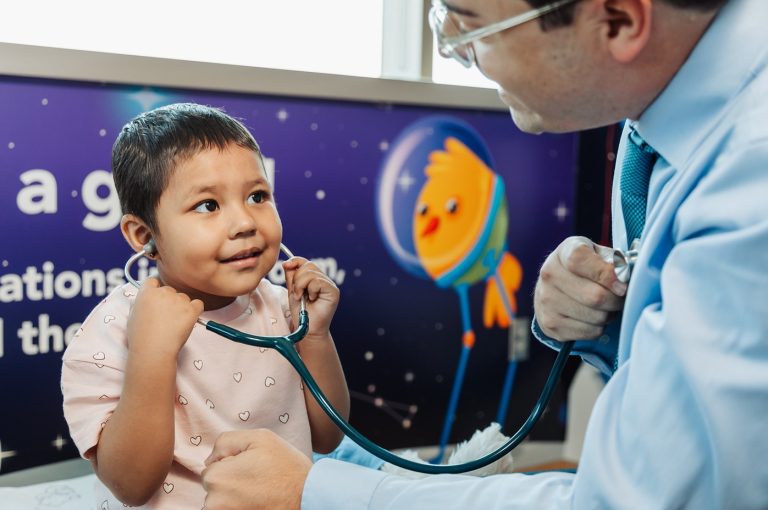 A toddler patient at Cure 4 The Kids Foundation holding a stethoscope with her oncologist, Dr. Raul
