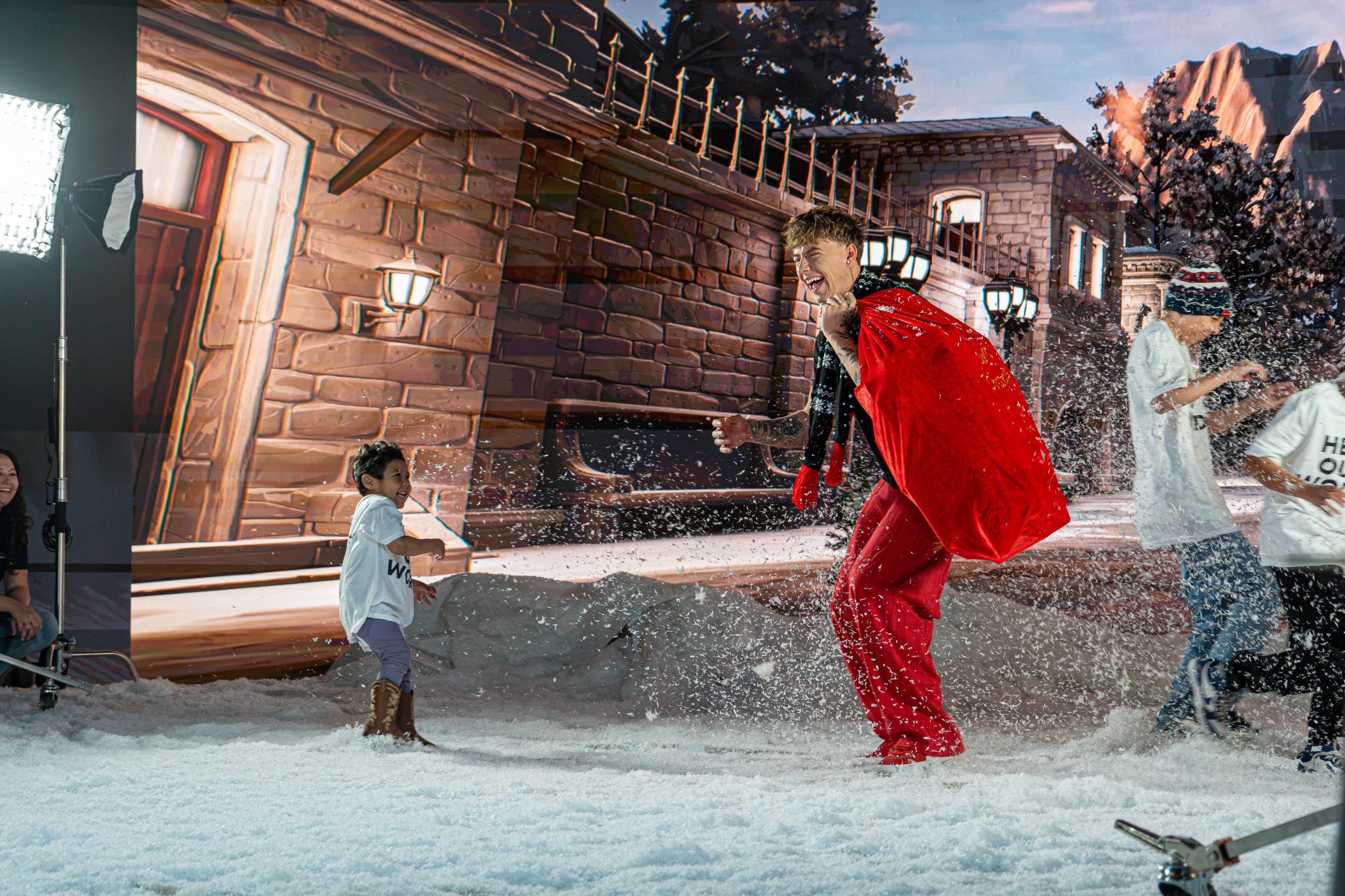 Mackenzie Sol, carrying a red gift sack, laughs with a small child as snow flies on the set