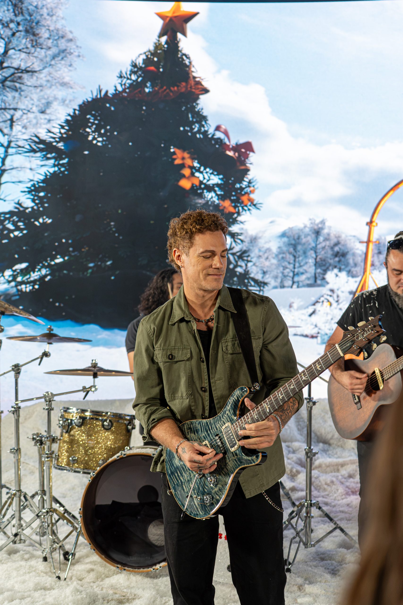 Miles Schon plays guitar in front of a snowy Christmas tree backdrop